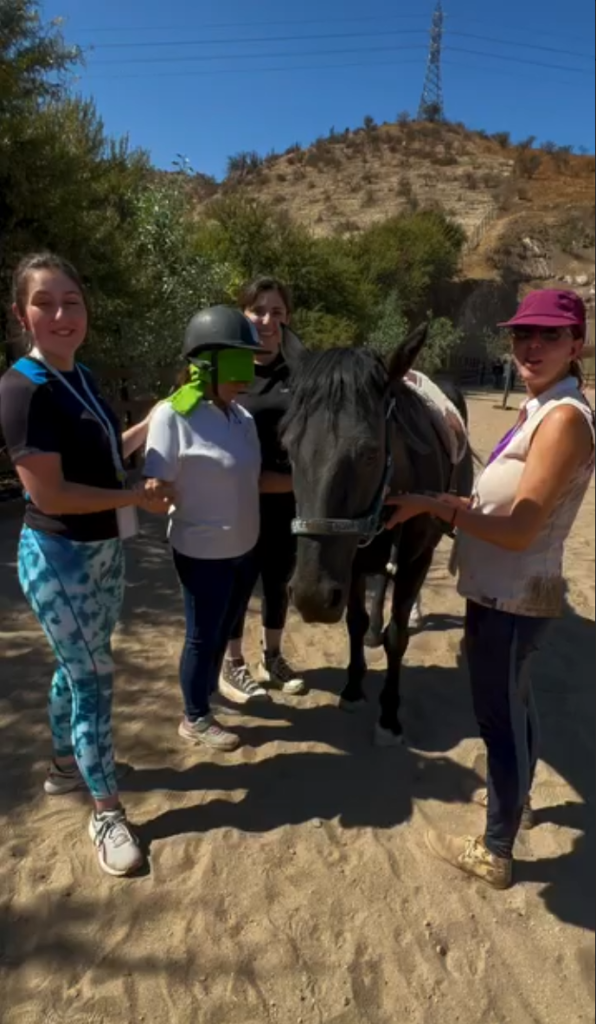 Alumnas y la instructora Eyleen realizando ejercicios de empatía con los ojos vendados junto a un caballo escuela en el Fundo Talanquén, Colina, durante marzo de 2024.